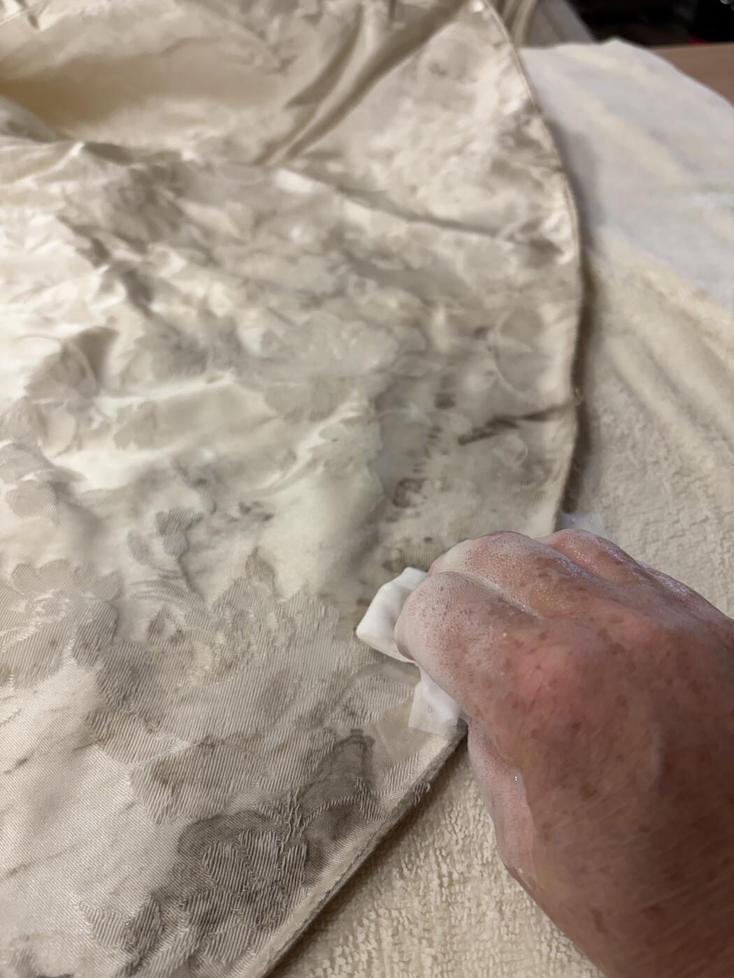Hand-dabbing an antique wedding dress hem with a soft cloth to lift staining