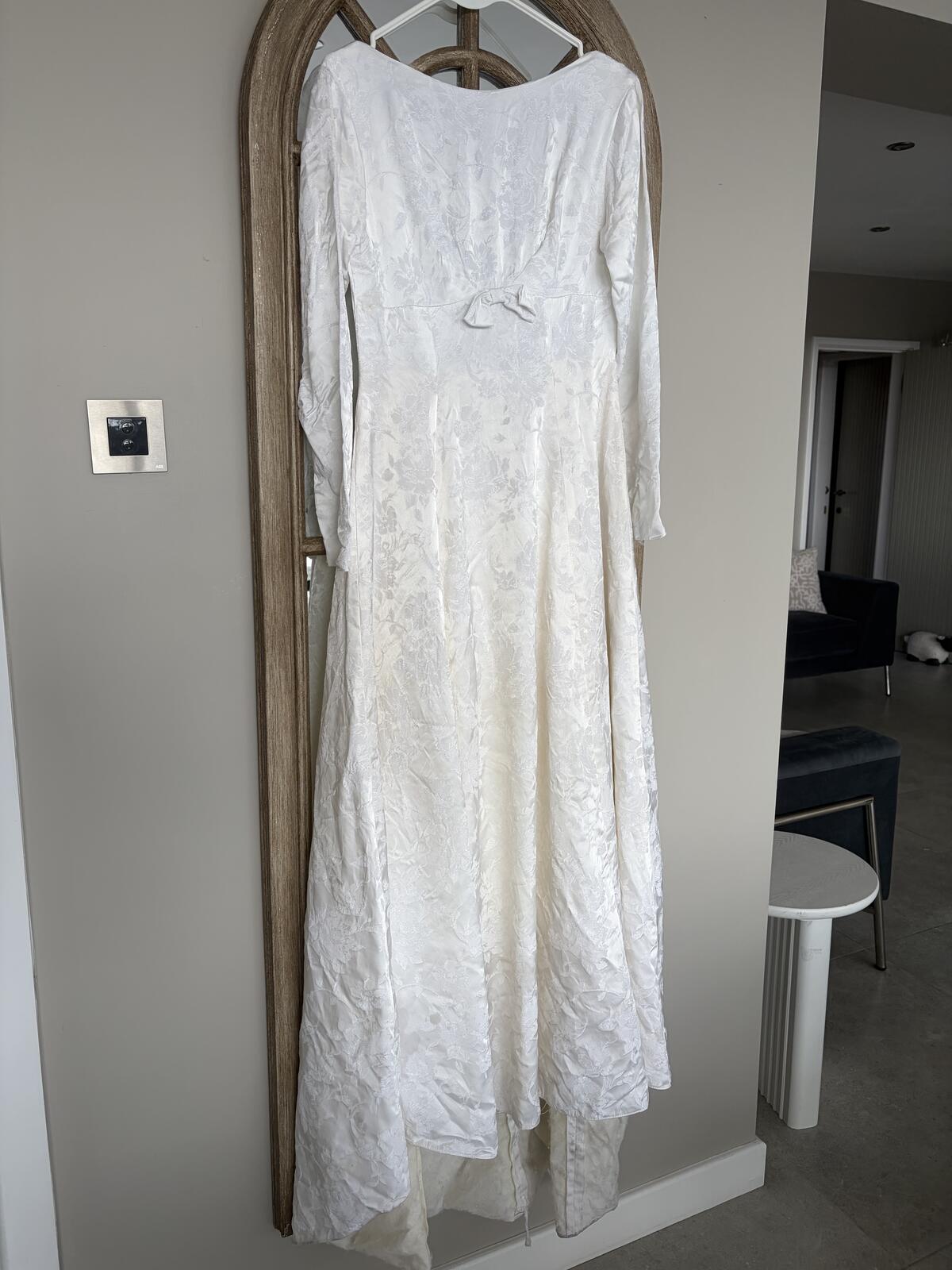 Restored antique floral jacquard wedding dress hanging in front of an arched mirror